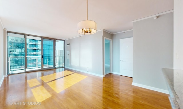 empty room featuring baseboards, ornamental molding, wood finished floors, expansive windows, and a notable chandelier