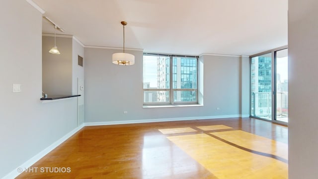 unfurnished room featuring ornamental molding, a wall of windows, baseboards, and wood finished floors