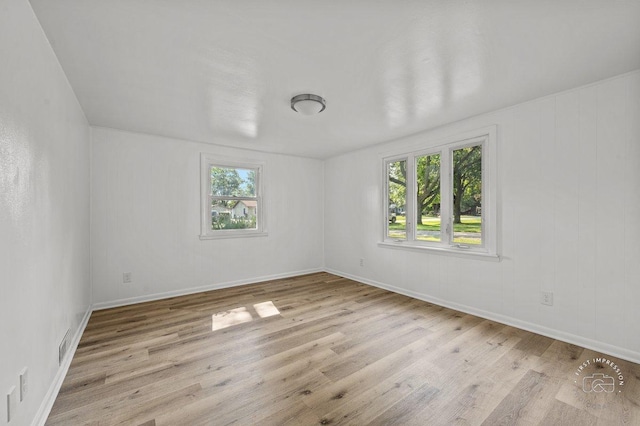 empty room featuring plenty of natural light, visible vents, baseboards, and wood finished floors