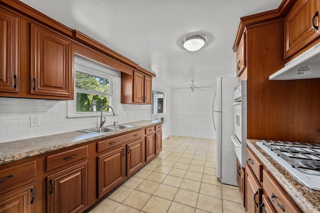 kitchen with light tile patterned flooring, gas cooktop, a sink, backsplash, and brown cabinets