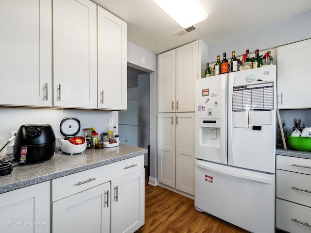 kitchen with visible vents, white refrigerator with ice dispenser, wood finished floors, and white cabinets