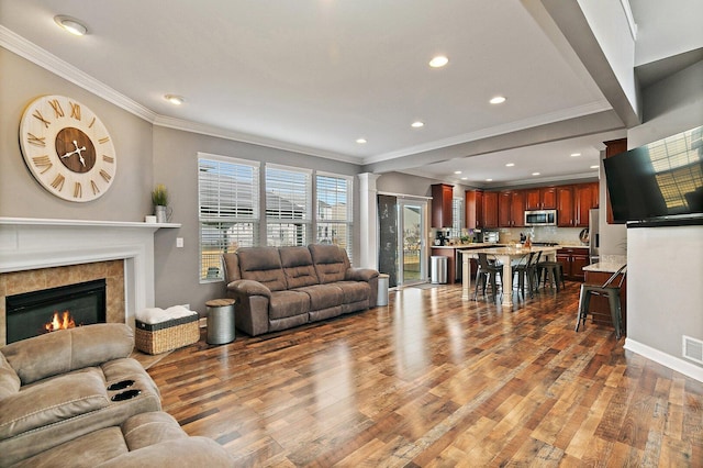 living room with visible vents, a tiled fireplace, ornamental molding, wood finished floors, and ornate columns