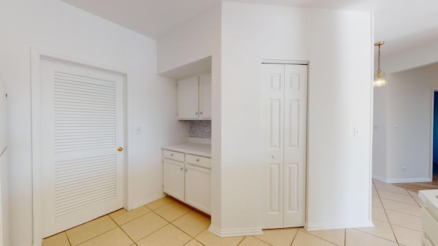 kitchen with pendant lighting, white cabinets, light countertops, light tile patterned floors, and baseboards