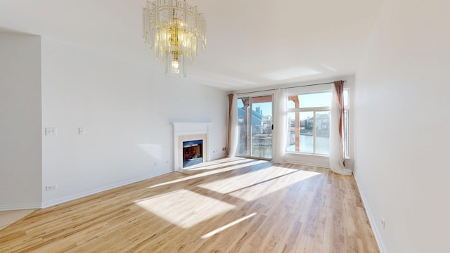 unfurnished living room featuring an inviting chandelier, light wood-style flooring, a fireplace, and baseboards