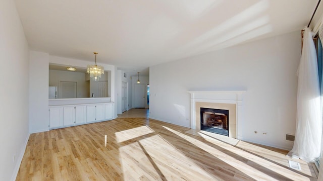 unfurnished living room with a fireplace with flush hearth, visible vents, baseboards, and light wood finished floors