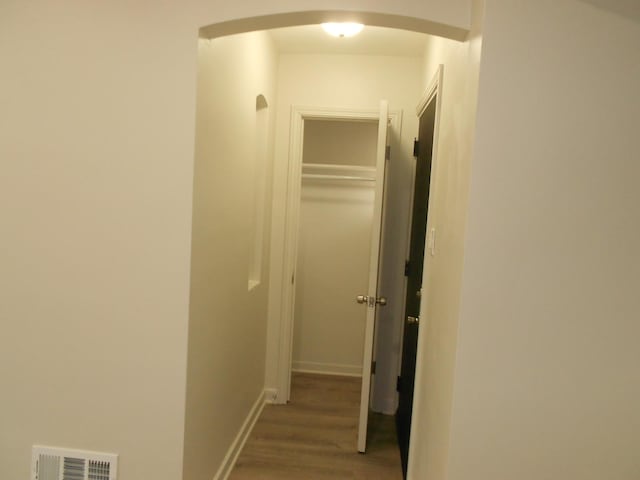 hallway featuring arched walkways, wood finished floors, visible vents, and baseboards