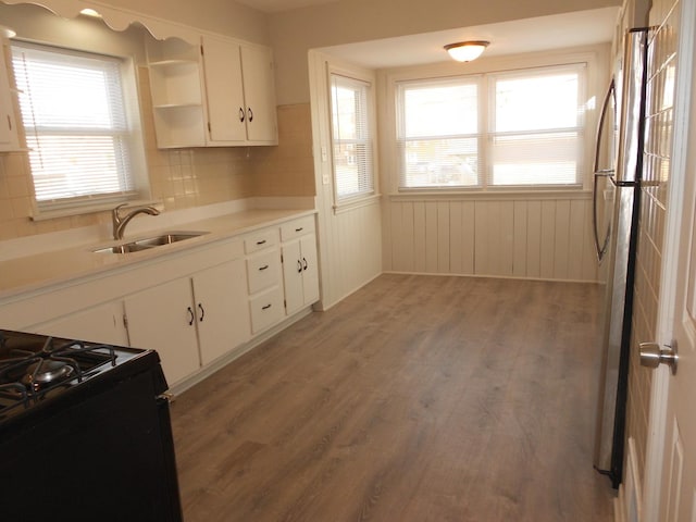 kitchen with light wood finished floors, black gas range oven, freestanding refrigerator, white cabinets, and a sink