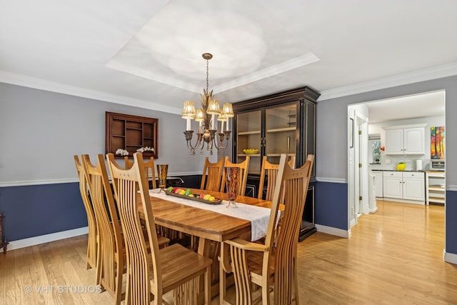 dining space featuring baseboards, a tray ceiling, crown molding, light wood-style floors, and a notable chandelier