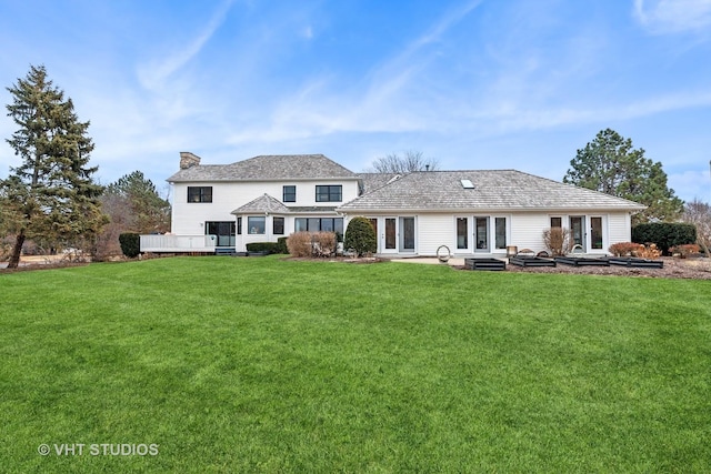 rear view of property featuring a deck, french doors, a chimney, and a lawn