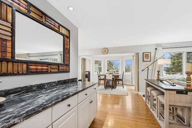 kitchen with a wealth of natural light, white cabinetry, light wood-style flooring, and dark stone countertops