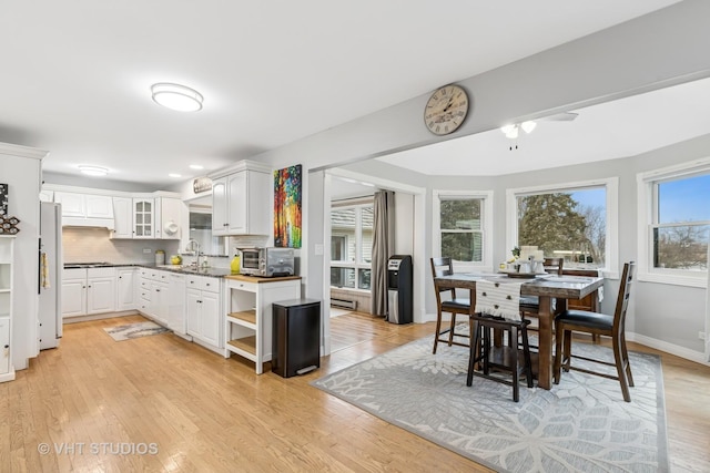 kitchen featuring white appliances, light wood finished floors, white cabinets, decorative backsplash, and a sink