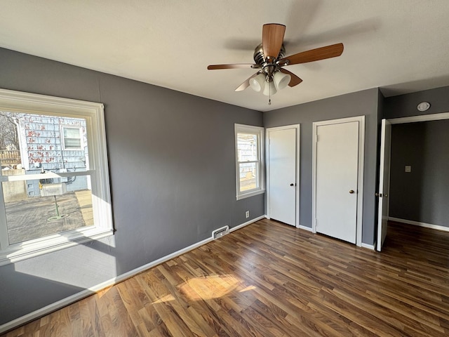 unfurnished bedroom with baseboards, visible vents, ceiling fan, wood finished floors, and two closets