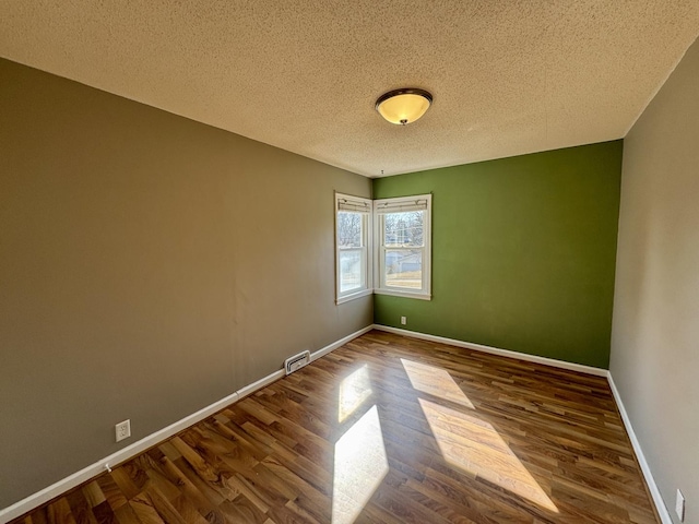 unfurnished room with baseboards, a textured ceiling, visible vents, and wood finished floors