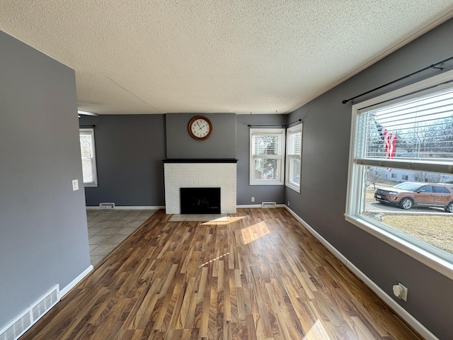 unfurnished living room with a wealth of natural light, a brick fireplace, visible vents, and wood finished floors