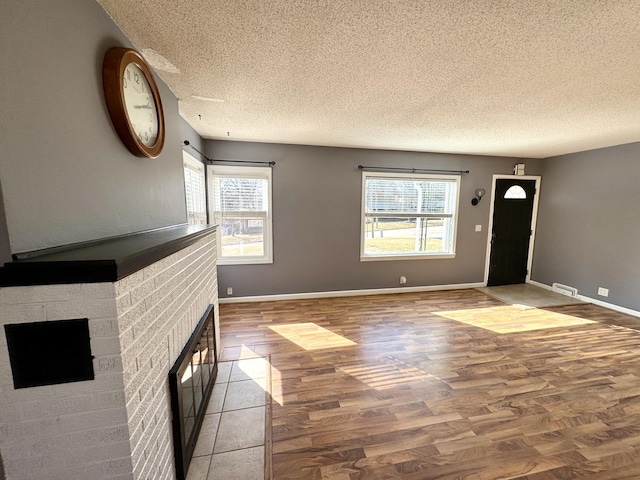 foyer entrance featuring a brick fireplace, a textured ceiling, baseboards, and wood finished floors