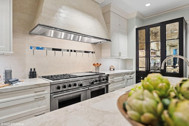 kitchen featuring tasteful backsplash, white cabinets, range with two ovens, ornamental molding, and wall chimney range hood