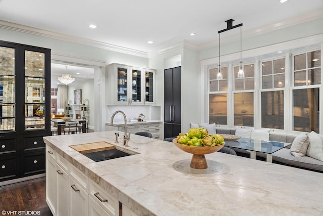 kitchen with dark wood-style floors, glass insert cabinets, ornamental molding, light stone countertops, and a sink