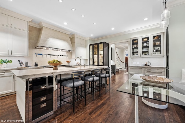 kitchen with beverage cooler, dark wood-style flooring, custom exhaust hood, an island with sink, and a kitchen bar