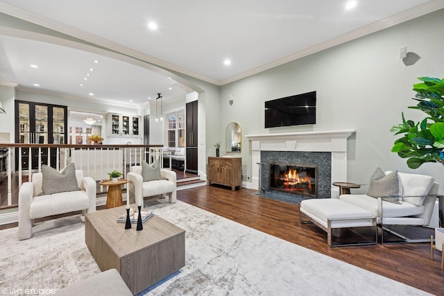 living area featuring a premium fireplace, recessed lighting, wood finished floors, and crown molding