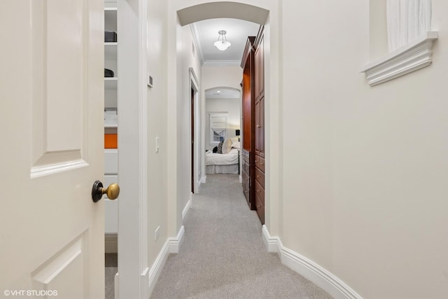 hallway with carpet floors, baseboards, arched walkways, and crown molding