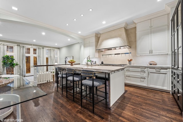 kitchen featuring an island with sink, dark wood-style floors, premium range hood, and a kitchen breakfast bar