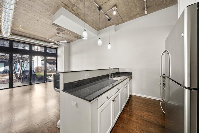 kitchen with dark wood finished floors, white cabinets, freestanding refrigerator, a peninsula, and a sink