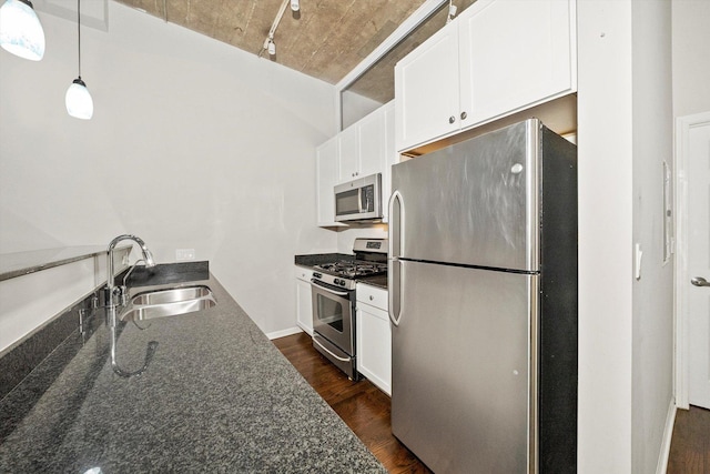 kitchen with dark wood finished floors, appliances with stainless steel finishes, white cabinets, a sink, and dark stone counters