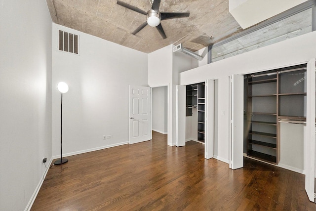 unfurnished bedroom featuring wood finished floors, a towering ceiling, visible vents, baseboards, and two closets