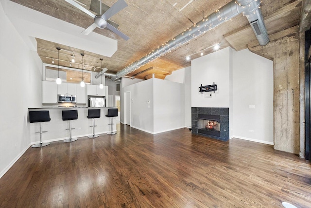 unfurnished living room with a fireplace, dark wood finished floors, rail lighting, a towering ceiling, and ceiling fan