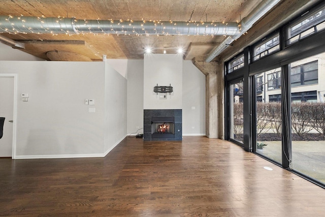 unfurnished living room featuring a fireplace, wood finished floors, a towering ceiling, and baseboards