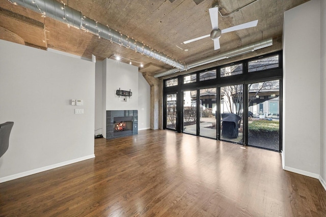 unfurnished living room with ceiling fan, a fireplace, baseboards, and wood finished floors