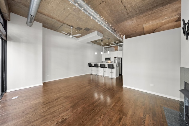 unfurnished living room with ceiling fan, dark wood-type flooring, and baseboards