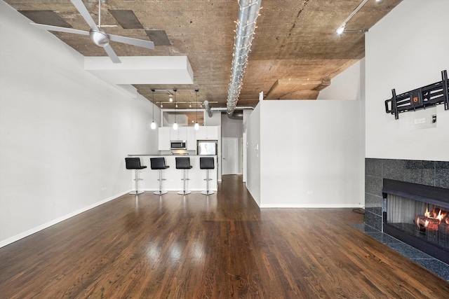 unfurnished living room with ceiling fan, a tiled fireplace, baseboards, and wood finished floors