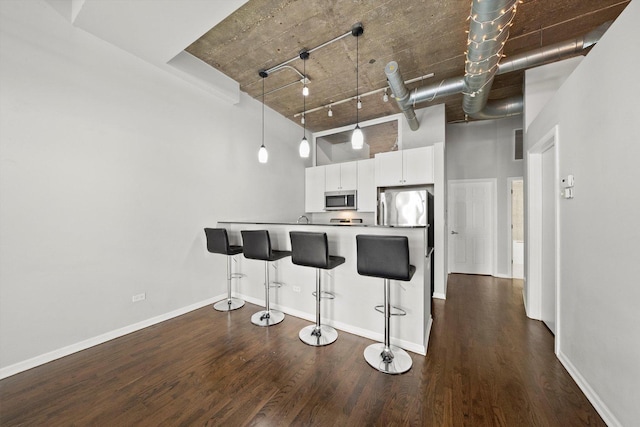 kitchen with dark wood-type flooring, a high ceiling, stainless steel appliances, a kitchen bar, and white cabinetry