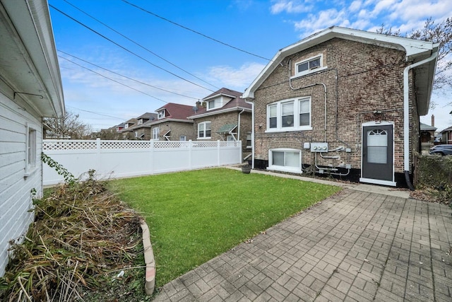 rear view of house with brick siding, a lawn, a fenced backyard, and a patio