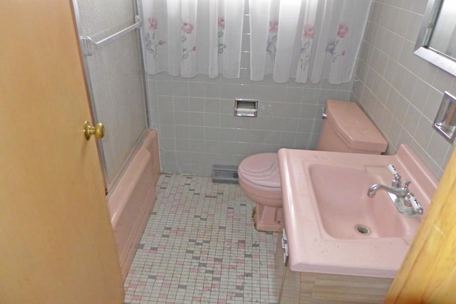 full bath featuring tile walls, bath / shower combo with glass door, toilet, a sink, and tile patterned flooring