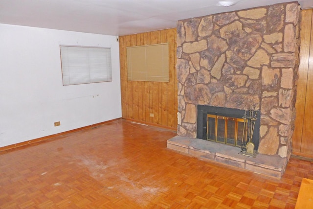 unfurnished living room with a fireplace, wooden walls, and baseboards