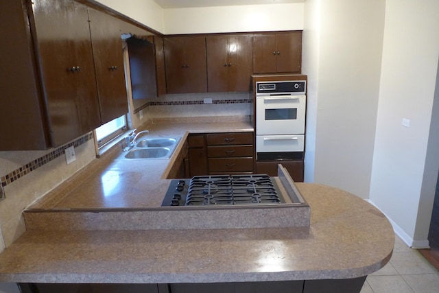 kitchen featuring light tile patterned floors, tasteful backsplash, a peninsula, stainless steel gas stovetop, and a sink