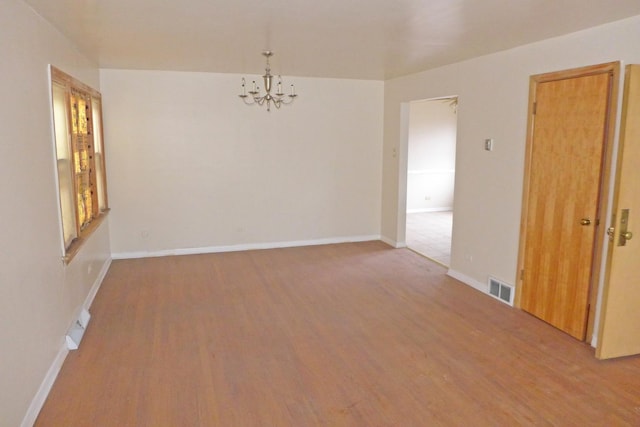 spare room with a chandelier, wood finished floors, visible vents, and baseboards