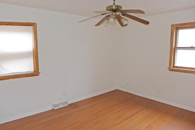 empty room with light wood finished floors, a ceiling fan, visible vents, and baseboards