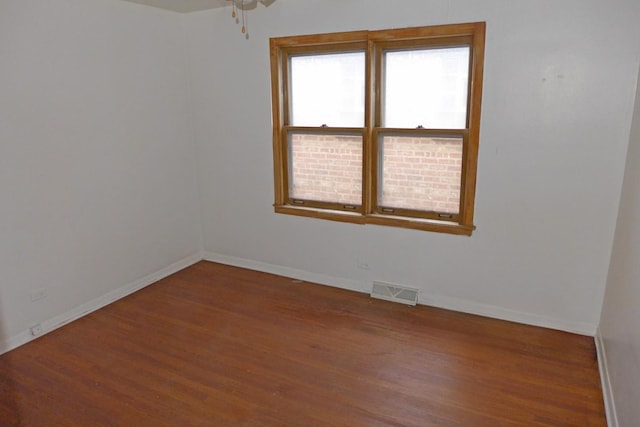 empty room featuring wood finished floors, visible vents, and baseboards