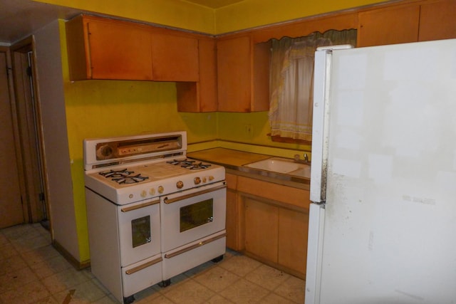 kitchen with light floors, white appliances, a sink, and brown cabinets