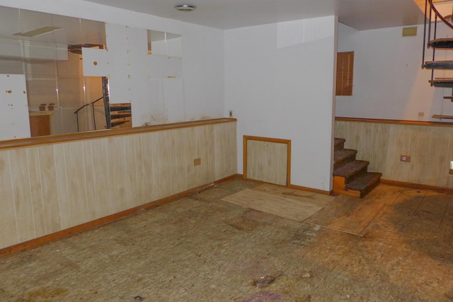 empty room with wooden walls, stairs, a wainscoted wall, and tile patterned floors