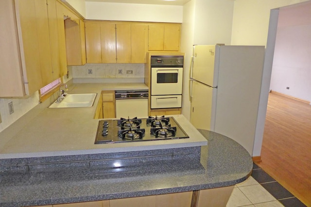 kitchen featuring tile patterned flooring, a peninsula, white appliances, a sink, and decorative backsplash