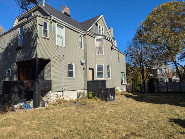 rear view of house with a chimney, fence, and a yard