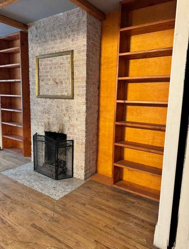 unfurnished living room featuring built in features, a brick fireplace, beamed ceiling, and wood finished floors