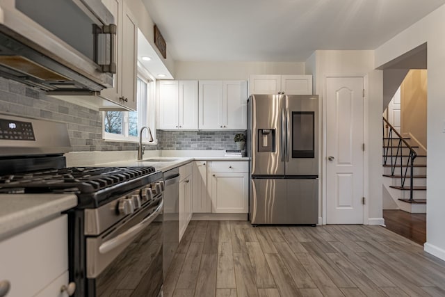 kitchen featuring light wood-style flooring, stainless steel appliances, light countertops, white cabinetry, and a sink