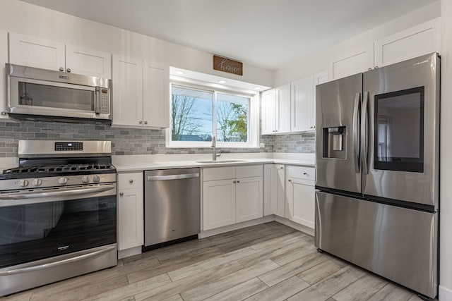 kitchen with light countertops, decorative backsplash, appliances with stainless steel finishes, white cabinets, and a sink