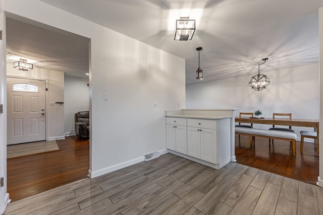 kitchen with wood finished floors, visible vents, baseboards, white cabinets, and light countertops