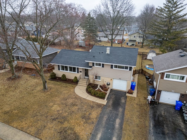 split level home featuring a garage, aphalt driveway, roof with shingles, and a residential view